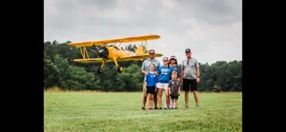 A family poses in front of a yellow biplane at a Carolina Aviators Network fly-in